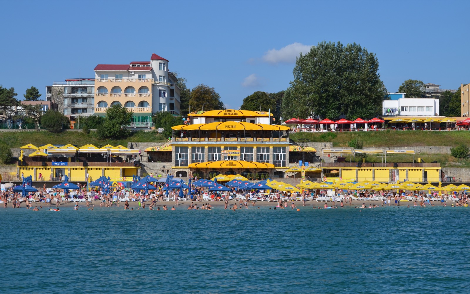 Plaja din Eforie Nord văzută dinspre mare, cu un restaurant galben pe nisip și hotelurile de pe faleză
