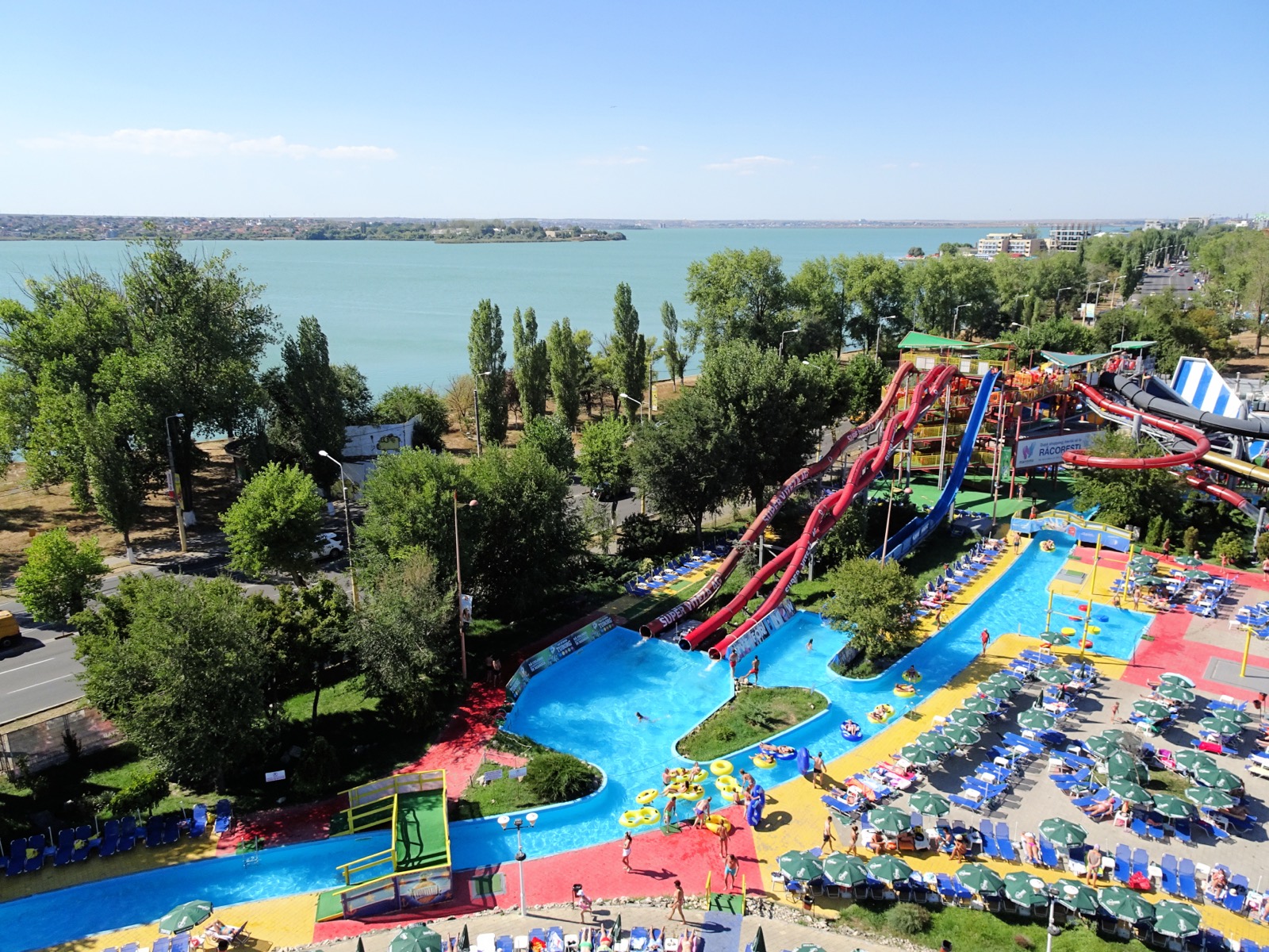 Toboganele roșii și albastre și râul leneș al parcului Aqua Magic, văzute de sus, cu lacul Siutghiol în fundal