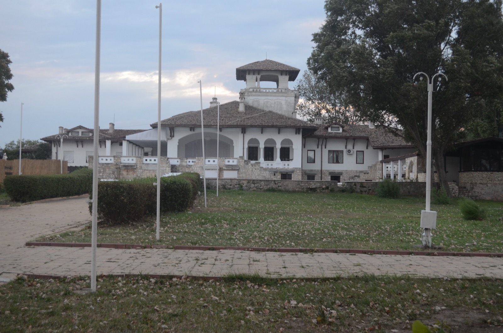 Fosta vilă regală din Mamaia, cu acoperiș de țiglă, foișor și arcade albe, în spatele unei peluze