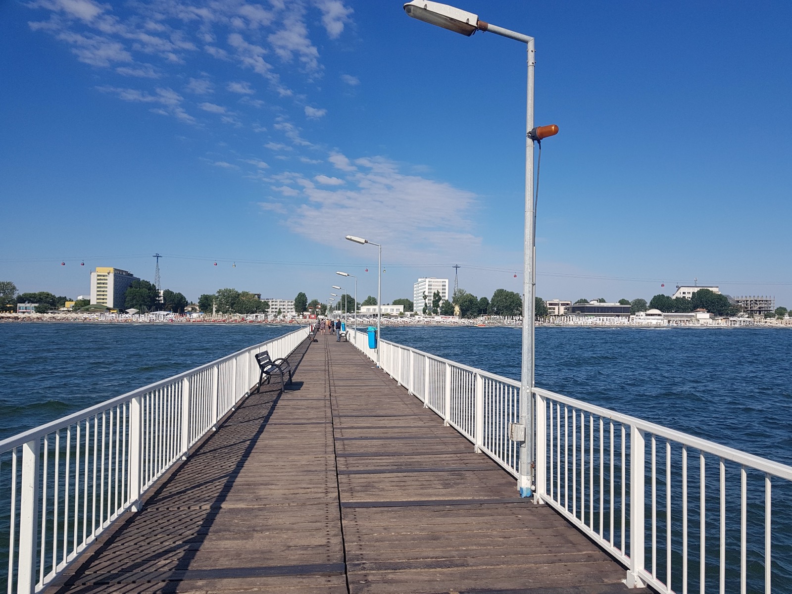 Die hölzerne Seebrücke, die ins Meer hinausführt, dahinter der Strand, die Hotels und die Kabinen der Seilbahn